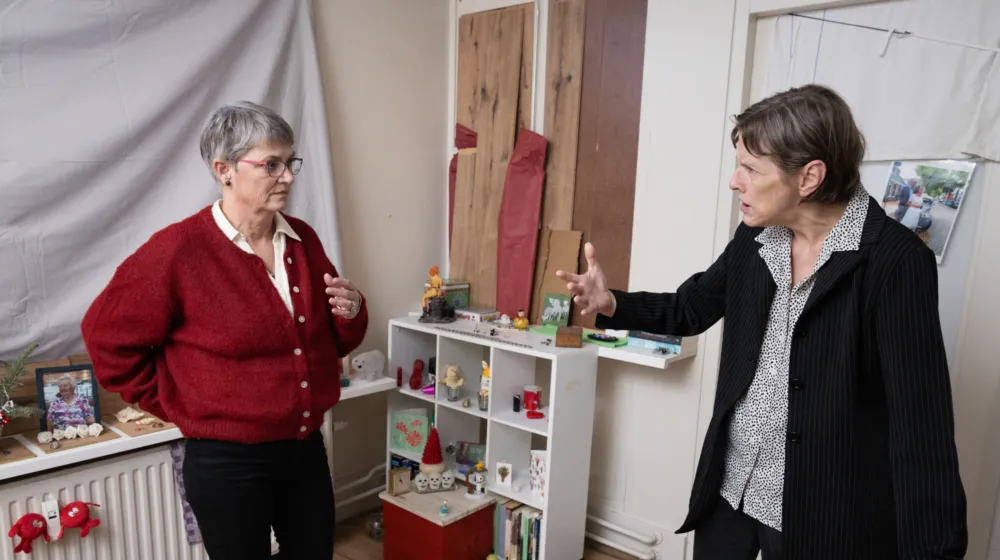 Twee vrouwen in een kamer samen in gesprek, op de achtergrond staan allerlei beeldjes in een kastje