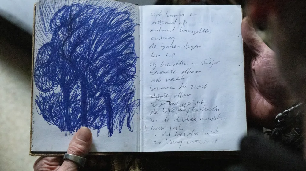 Iemand heeft een boekje in zijn hand. In het boekje staat links een pentekening van bomen en rechts staan niet goed leesbare aantekeningen