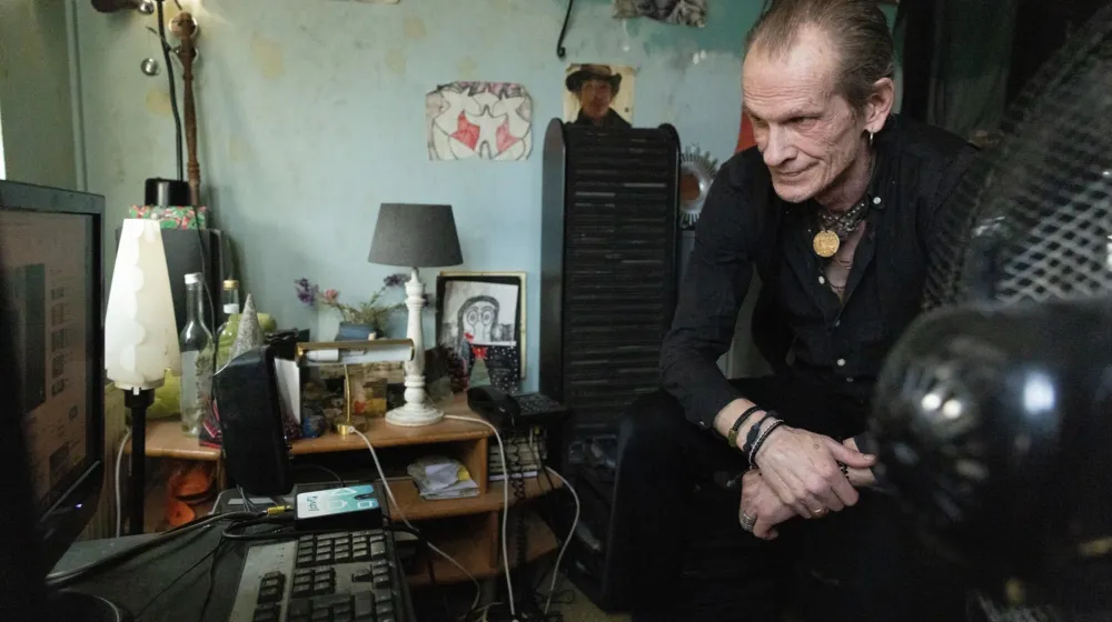 Man zit in zijn huiskamer en kijkt naar iets op het beeldscherm van zijn pc