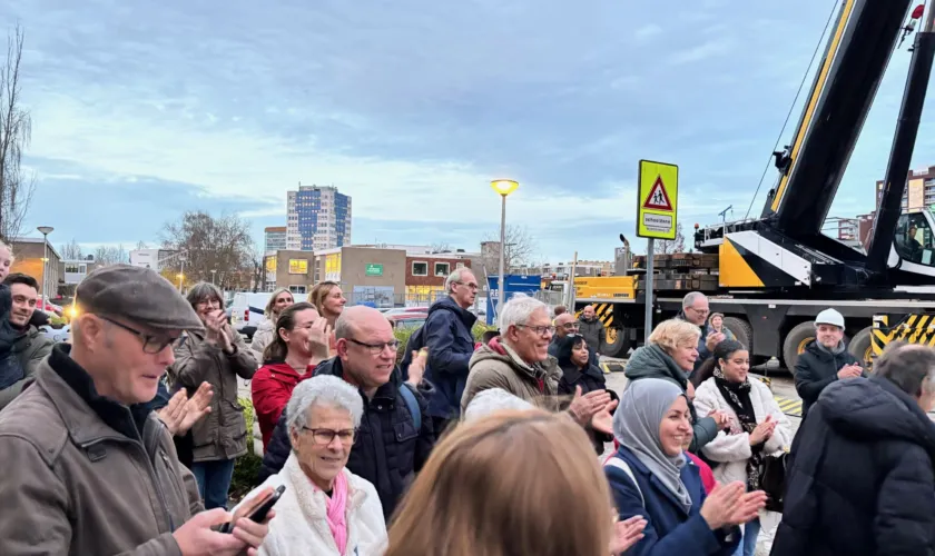 Een groep mensen staat buiten en applaudisseren. Op de achtergrond een grote bouwhijskraan.