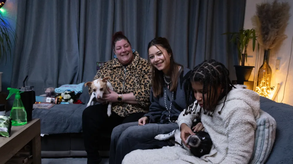 Een jongere met haar moeder en zusje, ze lachen en spelen met twee hondjes