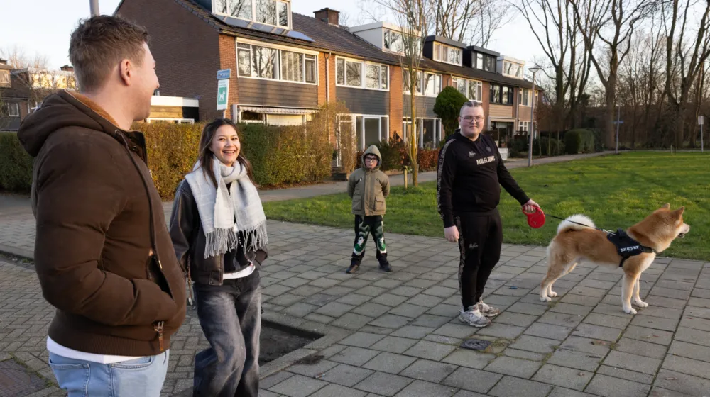 Drie jongeren laten een hond uit samen met de wooncoach, ze lachen naar elkaar