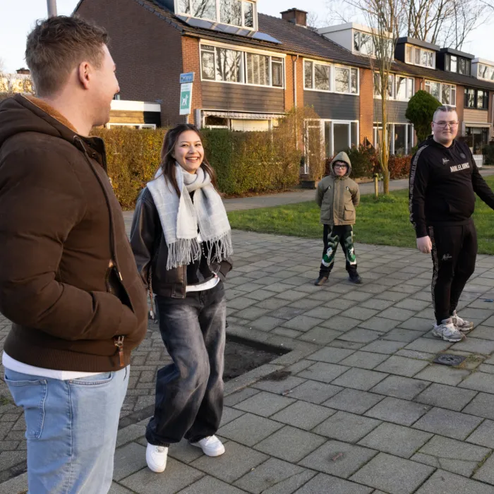 Drie jongeren laten een hond uit samen met de wooncoach, ze lachen naar elkaar