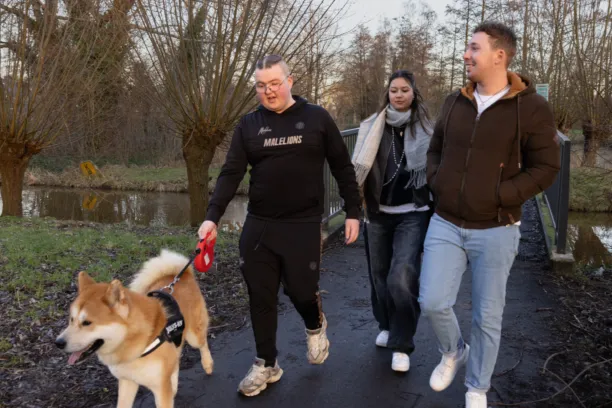 Twee jongeren en een wooncoach laten de hond uit, ze kletsen met elkaar