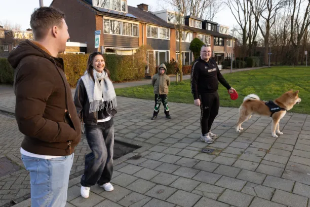 Drie jongeren laten een hond uit samen met de wooncoach, ze lachen naar elkaar