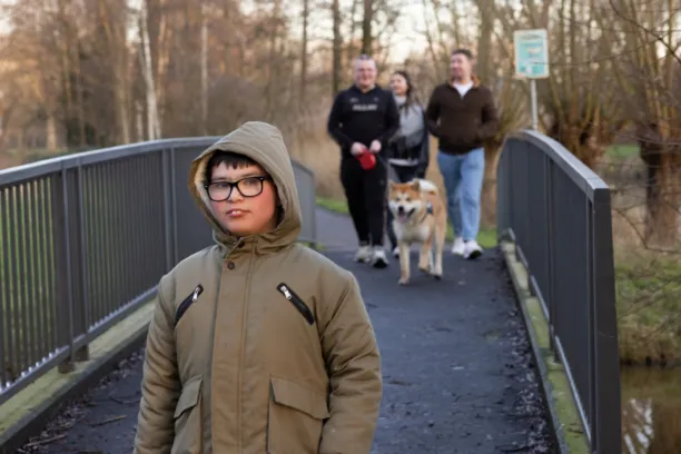 Een jongetje loopt buiten op een brug, achter hem drie mensen met een hond