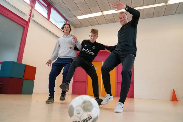 Twee sportcoaches van Pameijer en een jongen voetballen binnen in een sportzaal en hebben plezier