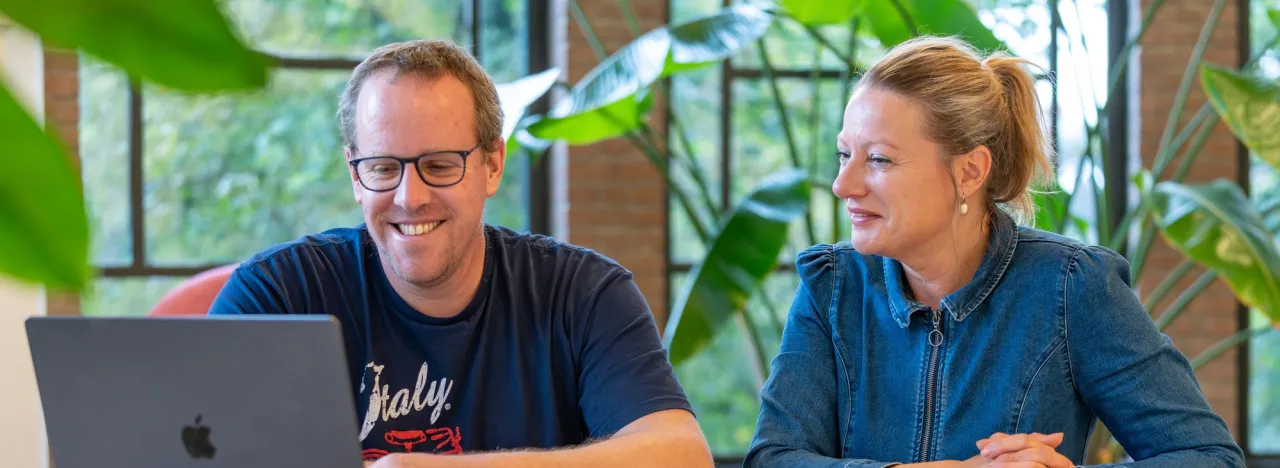 Een man en vrouw zitten samen achter een laptop en glimlachen allebei