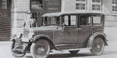 Oude foto van medewerker van de Buitendienst naast de auto waar hij huisbezoeken mee aflegt