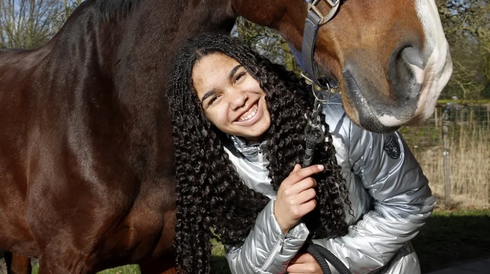 Lachend meisje heeft een paard vast aan het halstertouw