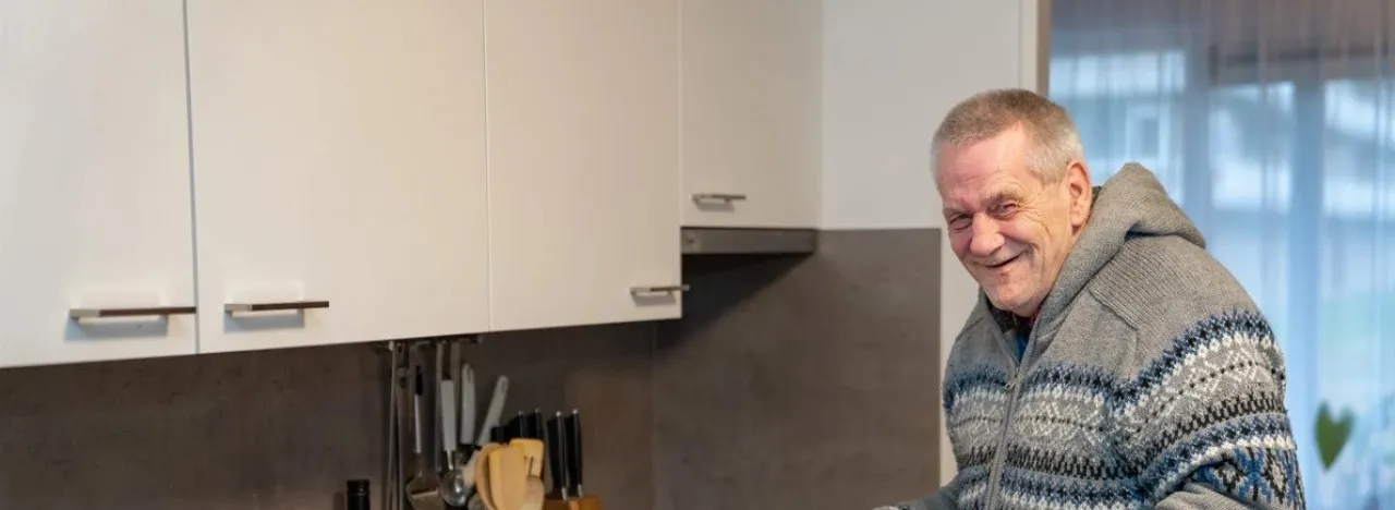 Man staat met een pan in de hand in een keuken en lacht naar de camera