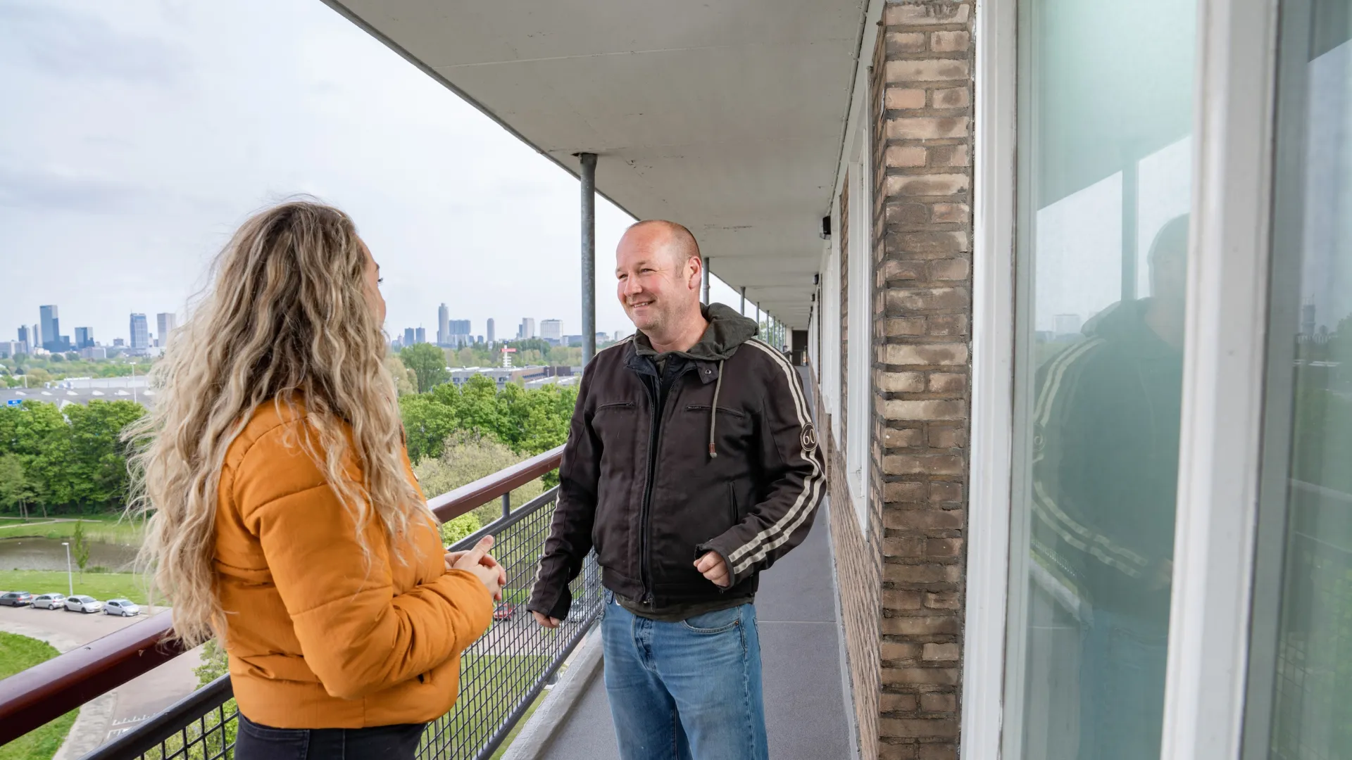 Twee personen staan op de galerij van een flat en zijn met elkaar in gesprek