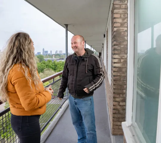 Twee personen staan op de galerij van een flat en zijn met elkaar in gesprek