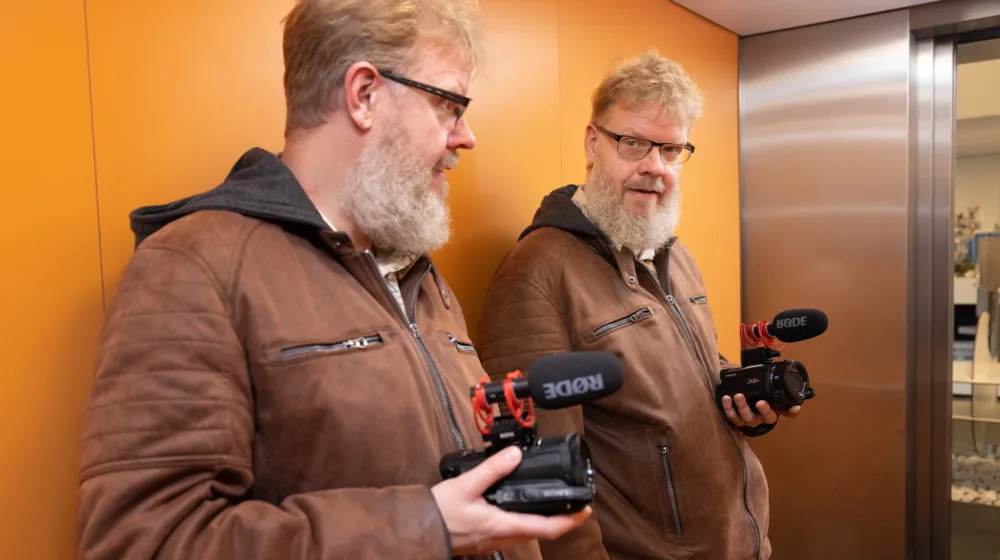 Man staat in de lift met een videocamera in zijn handen, hij kijkt in de spiegel