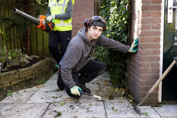 Man zit gehurkt en is onkruid aan het wieden terwijl hij de camera inkijkt