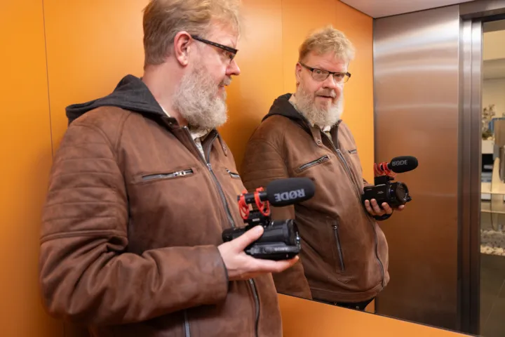 Man staat in de lift met een videocamera in zijn handen, hij kijkt in de spiegel