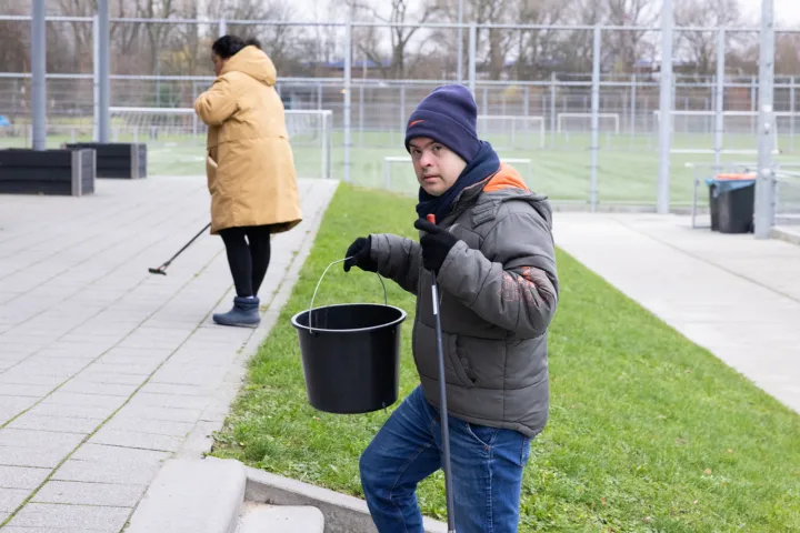 Man met emmer ruimt buiten op bij een voetbalclub