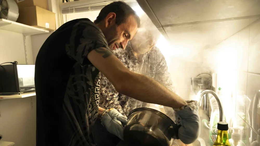 Twee mannen staan in de keuken en gieten het kookwater van de pan pasta af