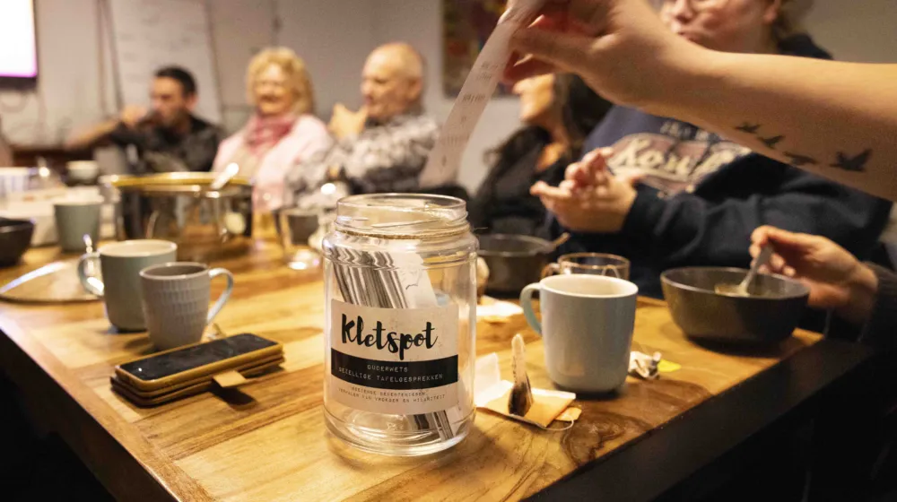 Mensen zitten met elkaar aan tafel, er wordt een kaartje toegevoegd aan de kletspot