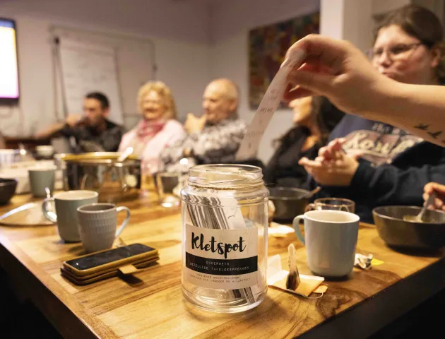 Mensen zitten met elkaar aan tafel, er wordt een kaartje toegevoegd aan de kletspot