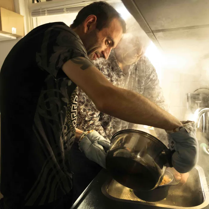 Twee mannen staan in de keuken en gieten het kookwater van de pan pasta af