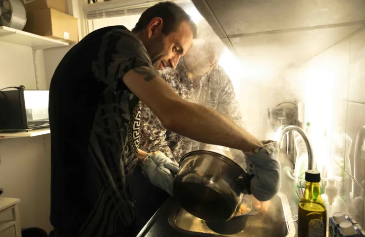 Twee mannen staan in de keuken en gieten het kookwater van de pan pasta af