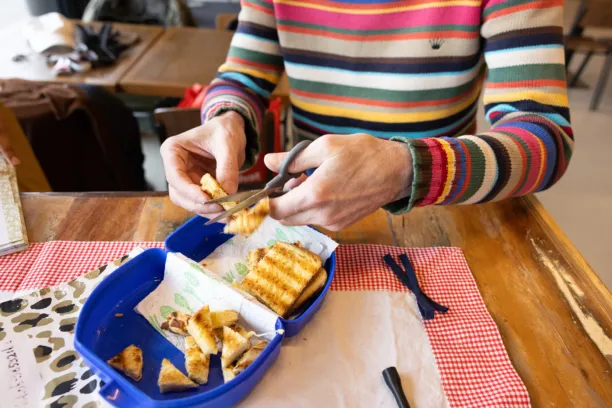 Iemand met een gestreepte trui knipt brood in stukjes in een blauwe broodtrommel