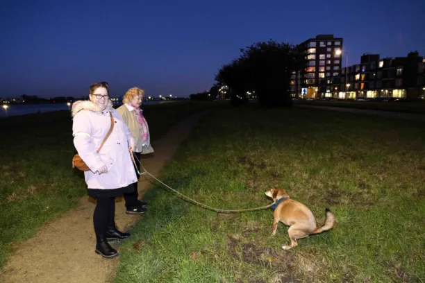 Twee vrouwen laten een hondje uit, het hondje poept, de vrouwen lachen