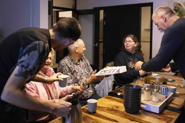 Mensen zitten met elkaar aan tafel er staat een soeppan en iemand deelt soep uit